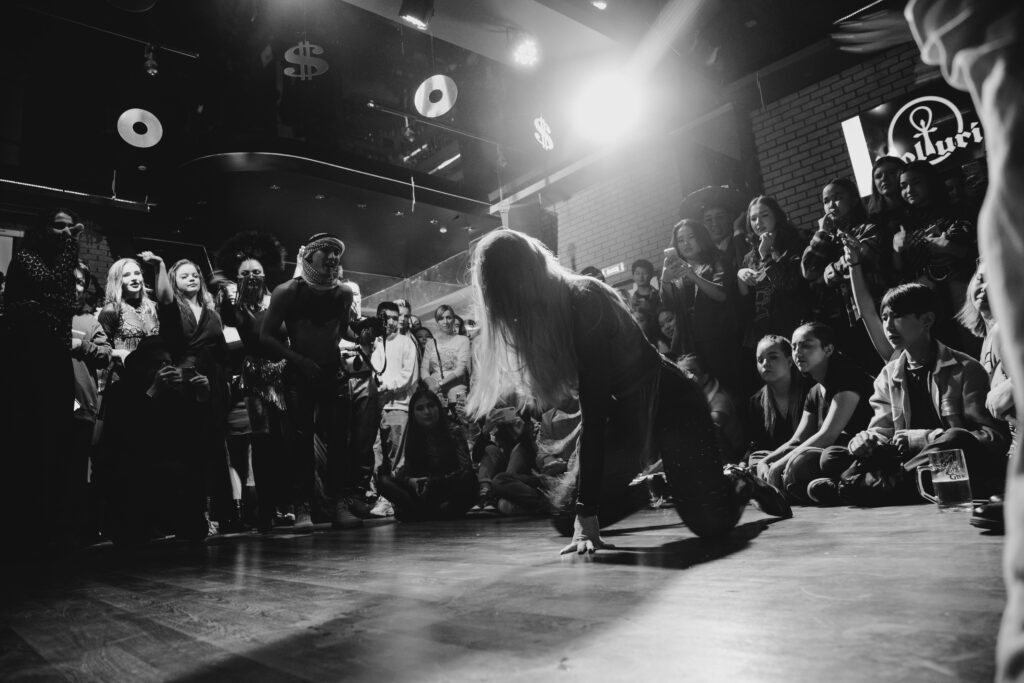 Dynamic black and white shot of a dancer performing to an enthralled crowd in a lively venue.